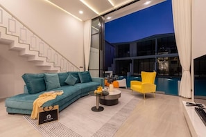 A modern living room with a teal sofa, a yellow armchair, a coffee table, and a staircase.