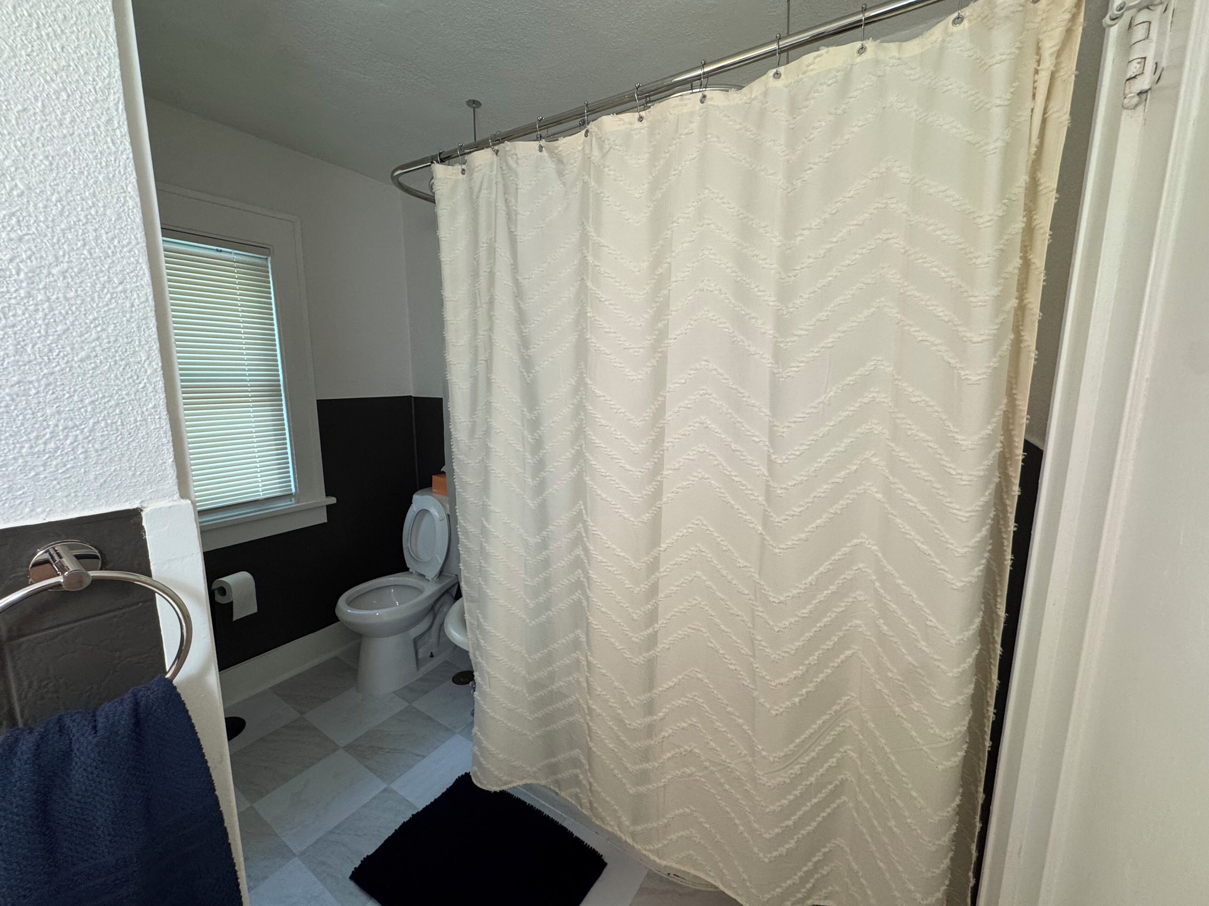 Ein Badezimmer mit weißer Duschvorhang, Toilette und einem Fenster mit Jalousien.