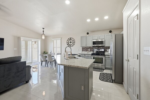 A modern kitchen with a central island, stainless steel appliances, and a dining area with chairs. - Sleek Modern Retreat w/ New Designer Kitchen & Private Turf (El Paso)