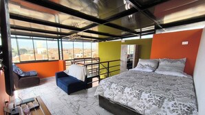 Een slaapkamer met een bed, een slaapbank, een kleine tafel met boeken en een balkon met een hekwerk.