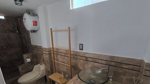 Een badkamer met een toilet, een glazen wastafel, een douche en een handdoekhouder.