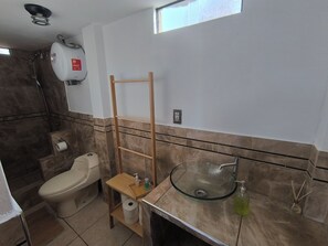 Ein Badezimmer mit Toilette, einem Waschbecken aus Glas, einer Dusche und einem Handtuchhalter.