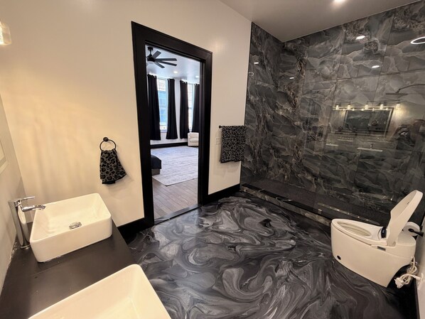 Ein modernes Badezimmer mit Marmorboden, einer weißen Badewanne, einer Toilette und einem schwarzen Waschtisch.