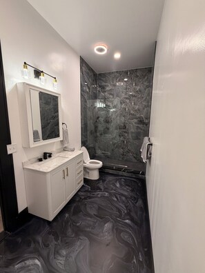 Ein Badezimmer mit Marmorboden, einem weißen Waschtisch mit Spiegel, einer Toilette und einer Duschkabine.