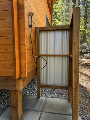Une cabane en bois avec une porte en métal, un tuyau fixé au mur et un chemin de gravier.