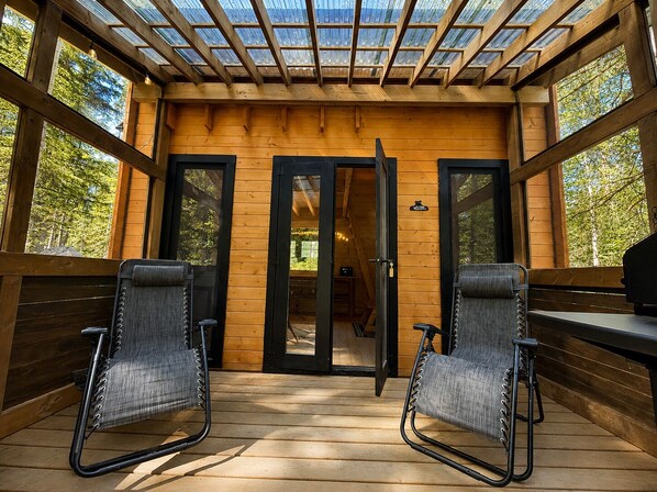Une terrasse en bois avec deux chaises, une porte et une vue sur l’extérieur.