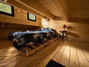 Une pièce de cabane en bois comprenant un lit, une petite table et une fenêtre.