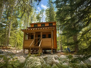 Une cabane en bois dotée d’un balcon, entourée d’arbres et de rochers.