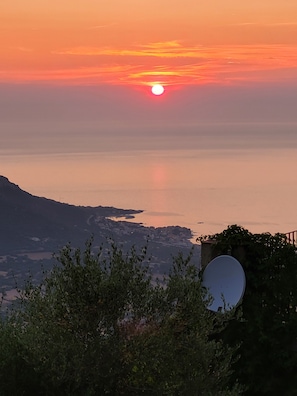 A sunset over a calm body of water with a mountain in the background. - Typical Corsican village. (Sant’Antonino)
