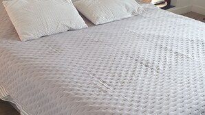 Een net opgemaakt bed met een ribbeltextuur witte deken, een houten hoofdbord en een nachtkastje met een lamp.