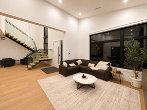 Ein modernes Wohnzimmer mit Treppe, einem Ecksofa, einem runden Couchtisch und einem großen Fenster.