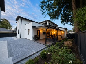 Ein modernes, zweistöckiges Haus mit überdachter Terrasse, Grill und einem angelegten Garten.