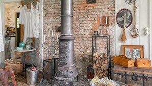 Una habitación rústica con un horno grande y decorativo, un cofre de madera y diversos objetos en estanterías y mesas.