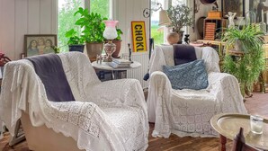 Una habitación acogedora con dos sillones blancos de mimbre, una mesa con libros y diversas plantas.