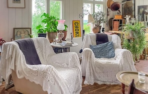 Ein gemütliches Zimmer mit zwei weißen Korbstühlen, einem Tisch mit Büchern und verschiedenen Pflanzen.
