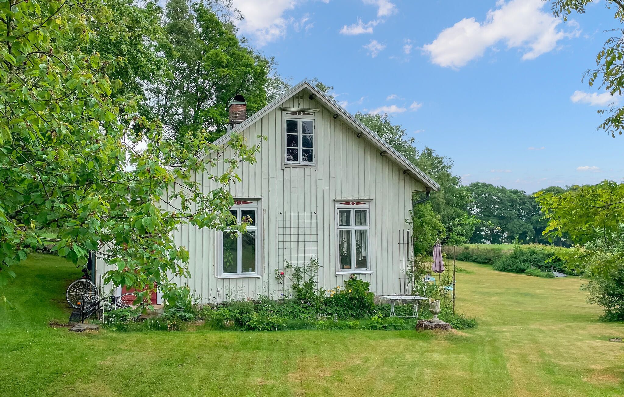 A white wooden house with a gabled roof, surrounded by a well-maintained lawn and trees.