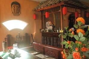 Ein traditionell eingerichteter Raum mit Holztisch, Buddha-Statue, Spiegel und roten Laternen.