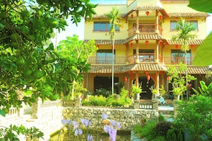 A multi-story building with balconies, a stone wall, and a water feature. - Art Rice field Y Van Cac Homestay  (Hoa Lu)