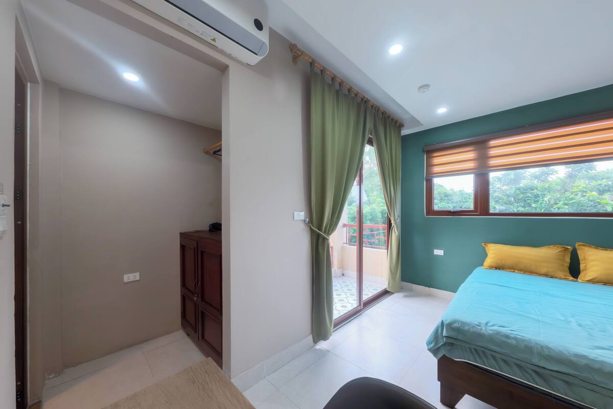 Un dormitorio con cama, escritorio, silla, armario y puerta corrediza de vidrio que da a un balcón.