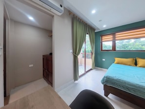 Ein Schlafzimmer mit Bett, Schreibtisch, Stuhl, Kleiderschrank und einer Glastür zum Balkon.