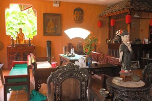 A traditional room with a Buddha statue, a green cushioned chair, a wooden table with a vase of flowers, and a decorative Buddha head. - Art Rice field Y Van Cac Homestay  (Hoa Lu)