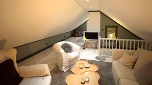 Ett mysigt sovrum på loftplan med ett sluttande tak, en tv och en trappa som leder upp till en övre våning.