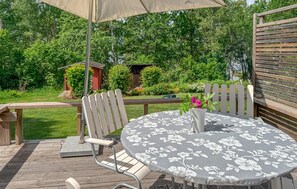 Eine Holzterrasse mit rundem Tisch und Stühlen, eine Pergola mit Markise und ein Garten mit Holzzaun und viel Grün.