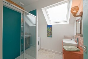 Ein modernes Badezimmer mit Oberlicht, einer Duschkabine aus Glas, einer Waschmaschine und einem Waschbecken mit einem dekorativen Spiegel.