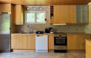 Eine Küche mit Holzschränken, einem Edelstahlkühlschrank, einer Spülmaschine, einer Kaffeemaschine und einem Herd.