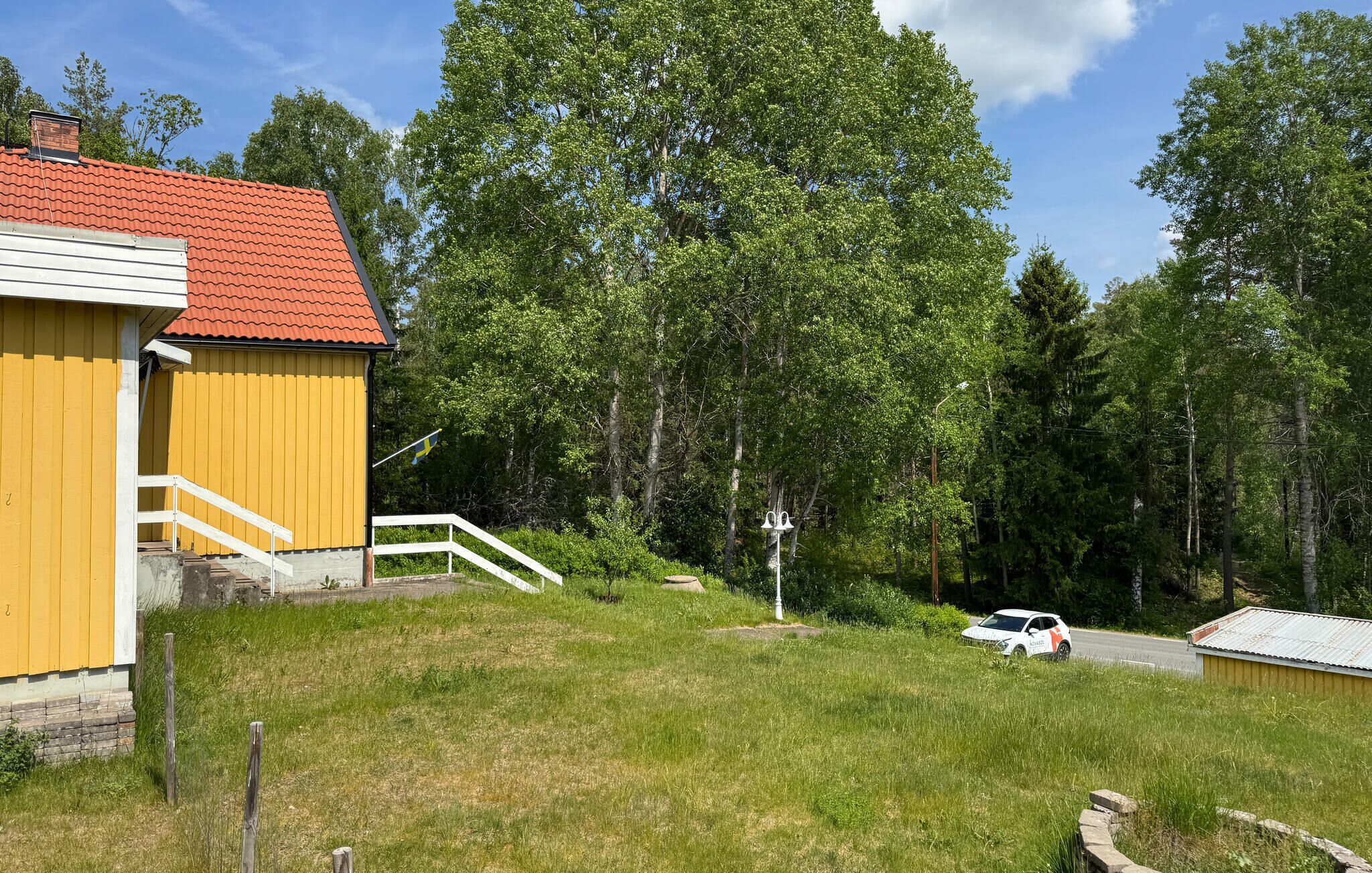 Un bâtiment jaune avec un toit rouge, un escalier blanc et une route où se trouve une voiture.