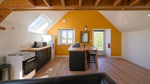 A kitchen with a stove, microwave, and wooden ceiling beams. - Balcony Cottage (Varouville)