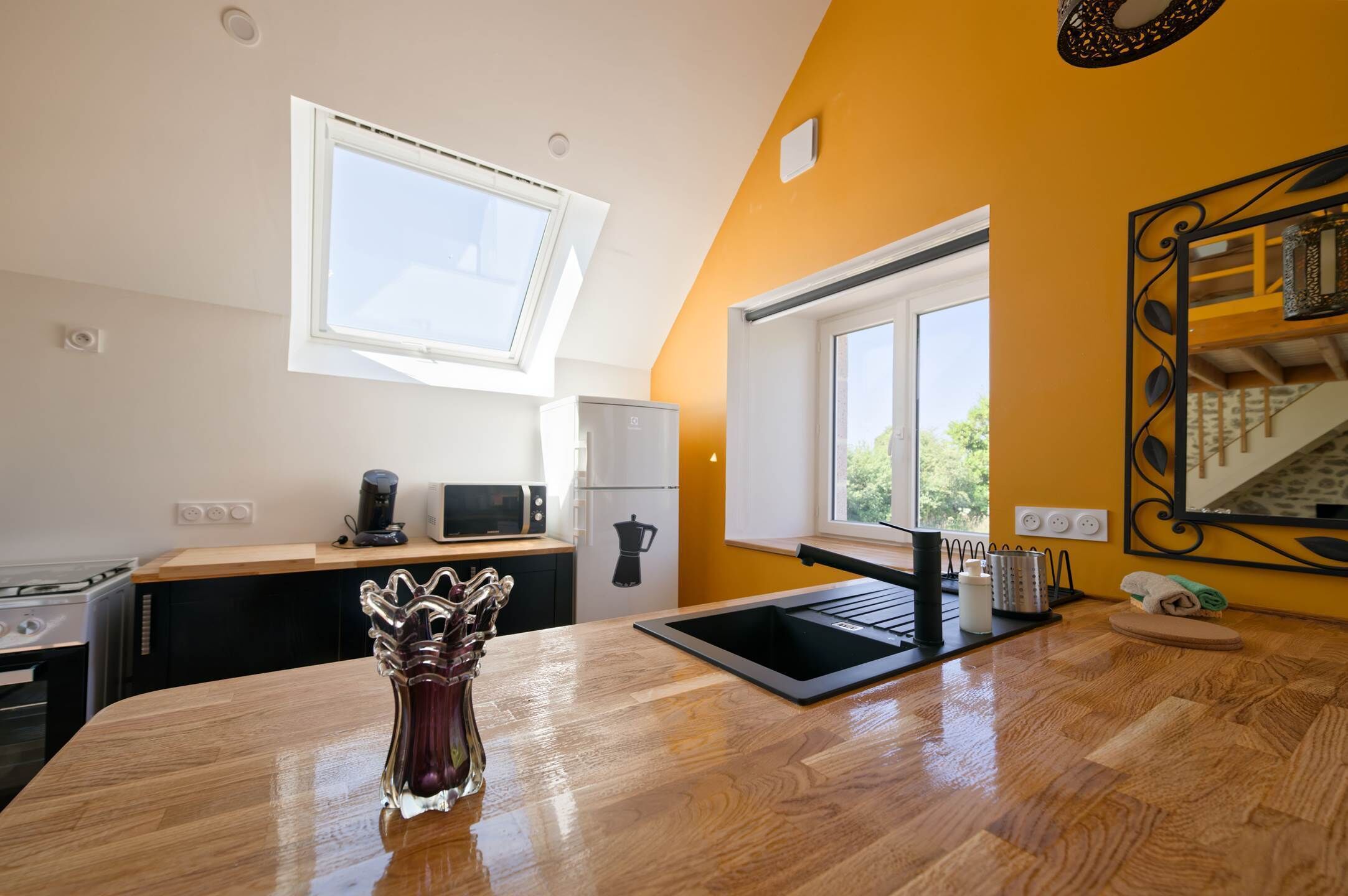 A kitchen with a wooden countertop, a sink, a window, and a microwave.