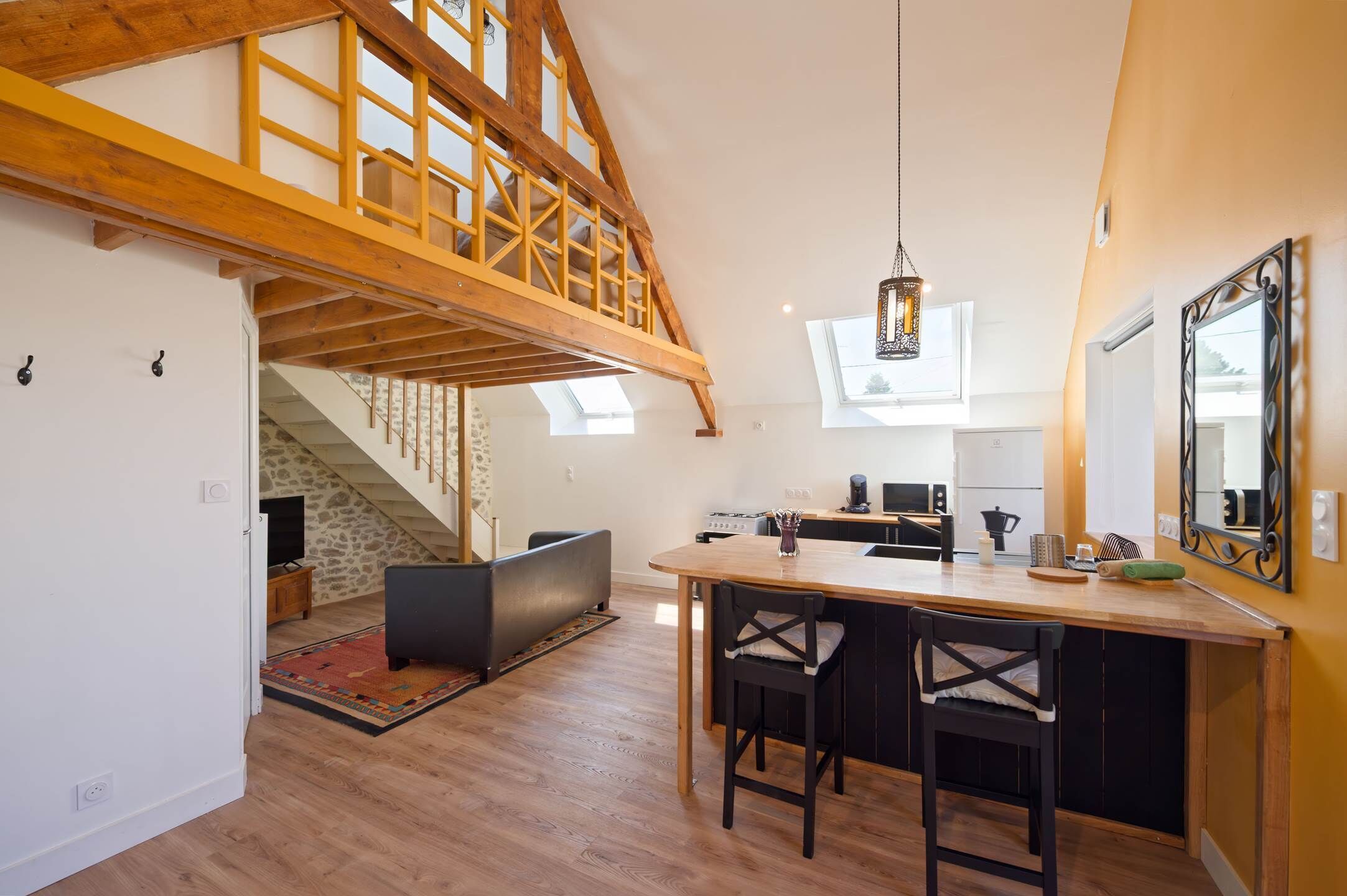 A spacious kitchen with a high ceiling, a dining area with two chairs, and a staircase leading to an upper level.
