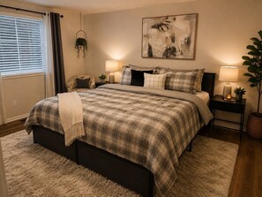 A bedroom with a bed, two bedside tables, a hanging plant, a painting, and a window with curtains. - Beautiful 3-bedroom house in tranquil Lithonia perfect for relaxing stays (Lithonia)