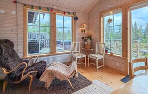 A cozy cabin interior with wooden walls, large windows, a fireplace, and a dining area. - Lovely apartment in Sälen with sauna (Sälen)