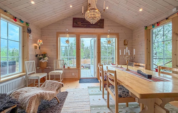 A wooden cabin interior with a dining table, chairs, a chandelier, and large windows. - Lovely apartment in Sälen with sauna (Sälen)