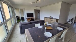 Un espai de vida modern amb zona de menjador, sofà, televisió, cuina i portes corredisses de vidre.