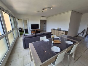 A modern living space with a dining area, sofa, TV, kitchen, and sliding glass doors. - 2 bedrooms, air-conditioned, WiFi, sea view, swimming pool (ST MANDRIER SUR MER)