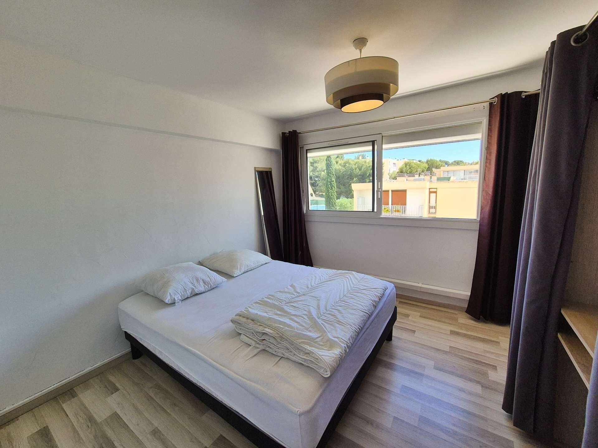 Une chambre à coucher avec un lit, une fenêtre, des rideaux et un luminaire au plafond.