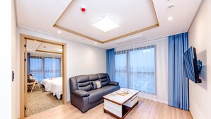 Ein modernes Hotelzimmer mit Sofa, Couchtisch, Fernseher und einem großen Fenster mit Vorhängen.