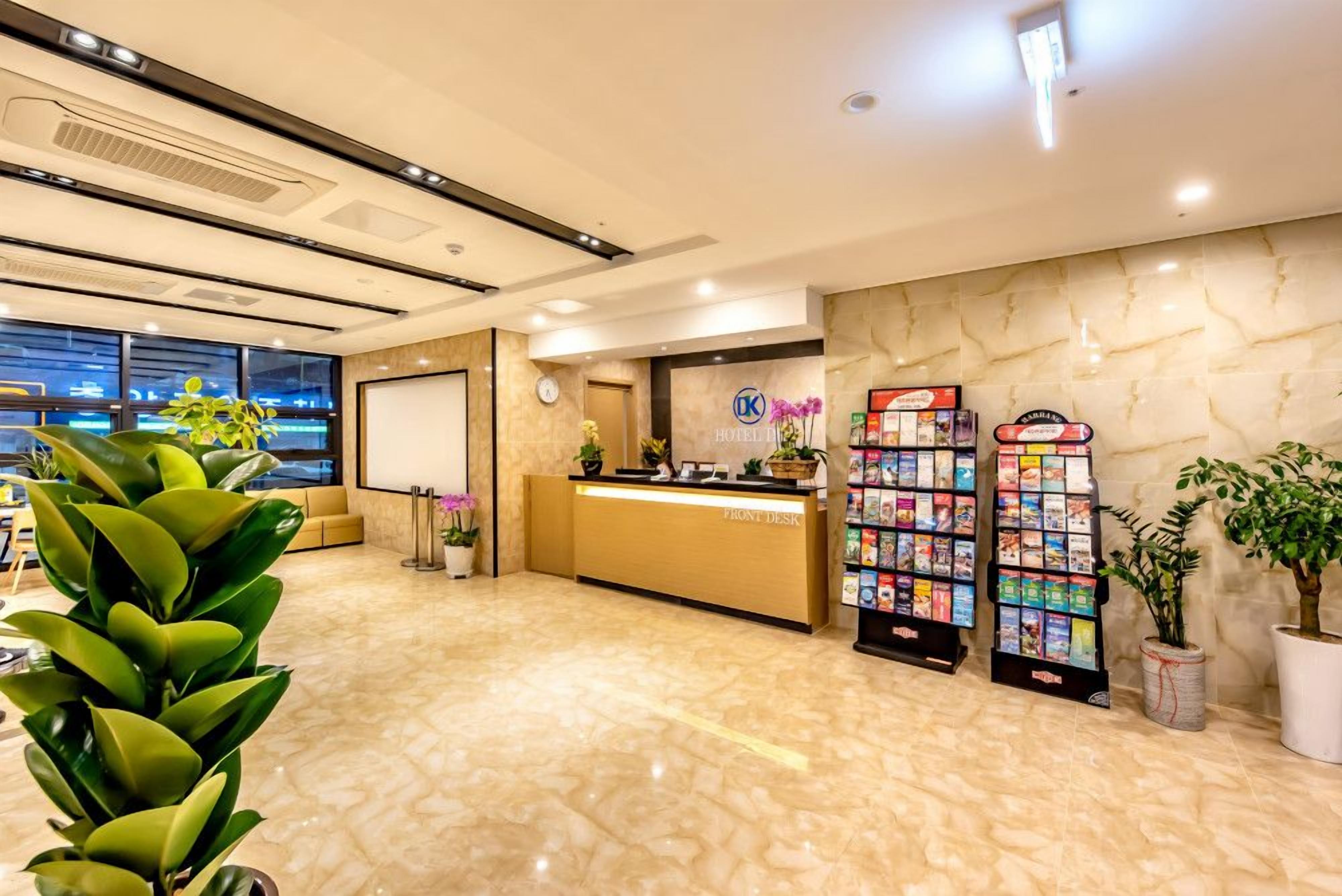 Uma área de recepção de hotel com piso de mármore, balcão de atendimento, relógio e porta-revistas.
