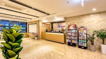 Uma área de recepção de hotel com piso de mármore, balcão de atendimento, relógio e porta-revistas.