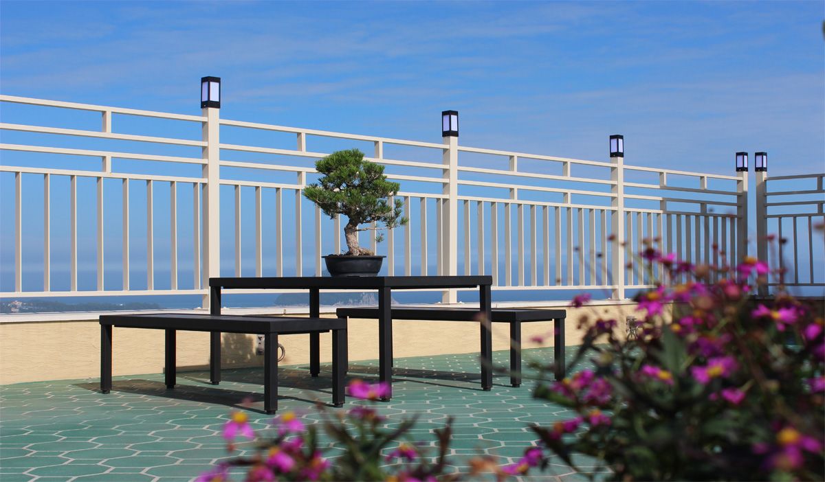 Terraço com bonsai em vaso, um banco e guarda-corpo com lanternas.