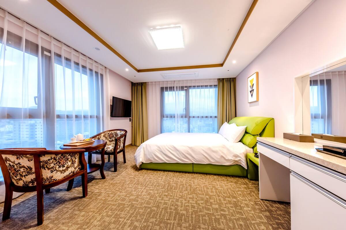 A hotel room with a bed, a desk, a chair, a television, and large windows.