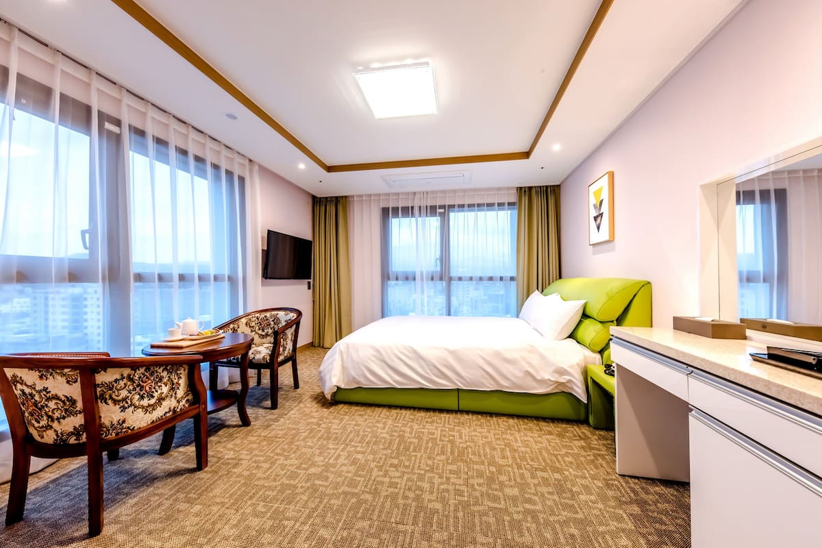 A hotel room with a bed, a desk, a chair, a television, and large windows.