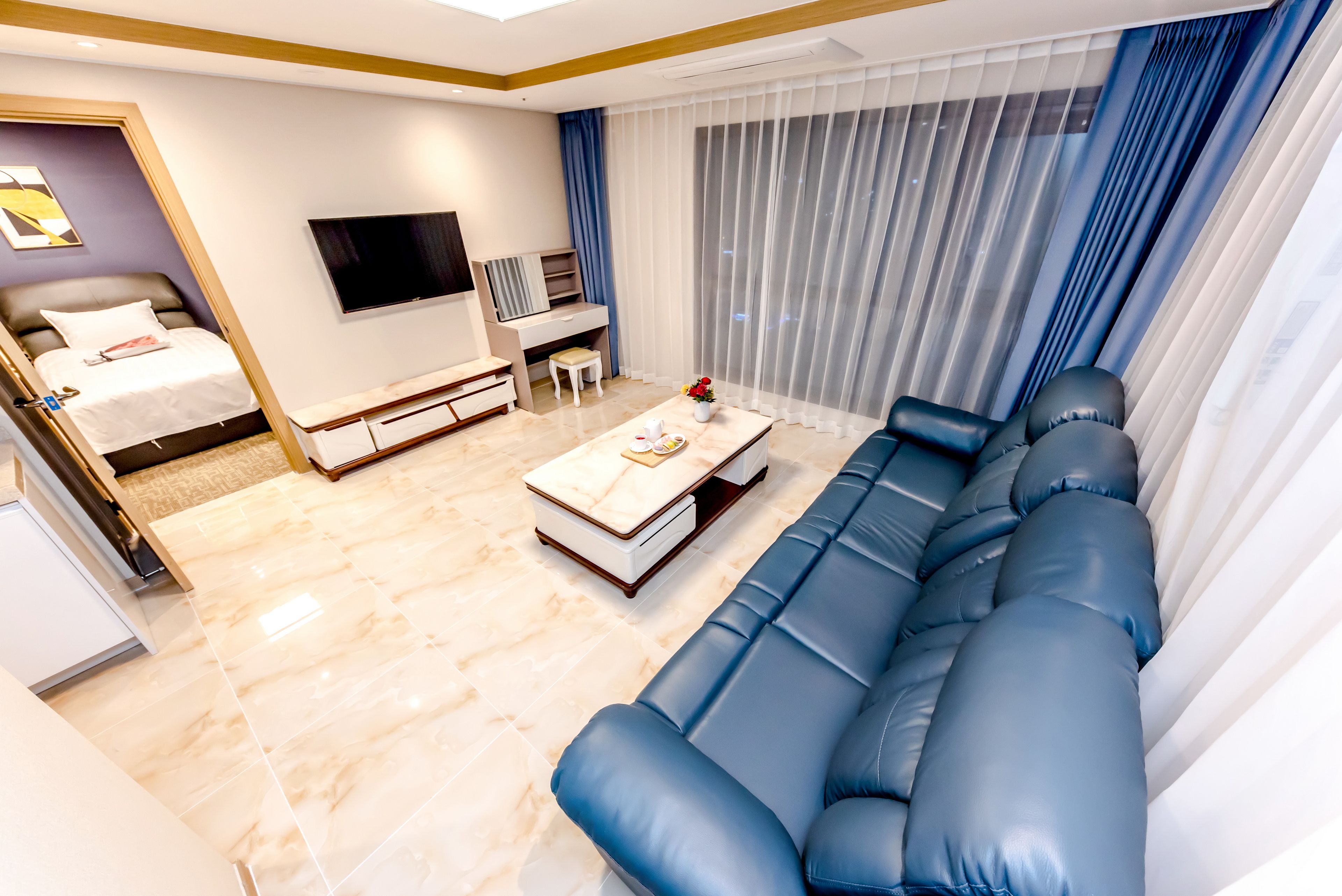 Una sala de estar moderna con un sofá, televisión, mesa de centro y cama.