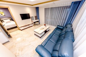 A modern living room with a sofa, a TV, a coffee table, and a bed. - HOTEL DK (Seogwipo)
