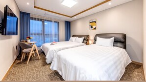 Ein Hotelzimmer mit zwei Betten, einem Schreibtisch, einem Sessel, einem Fernseher und einem Fenster mit Vorhängen.