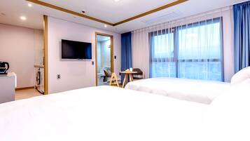 Habitación de hotel con dos camas, televisión, una mesita y vista a la ciudad desde la ventana.