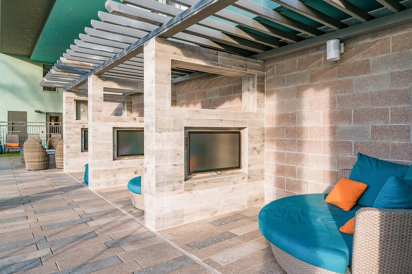 An outdoor patio with a stone wall, a pergola, and a seating area with cushions.